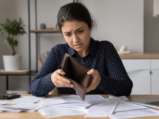 Person holding an empty wallet with a worried expression, surrounded by unexpected bills, representing hidden migration costs.